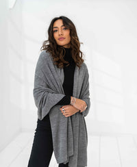 Merino wool maxi scarf in light grey melange, shown draped over shoulders in a bright room.