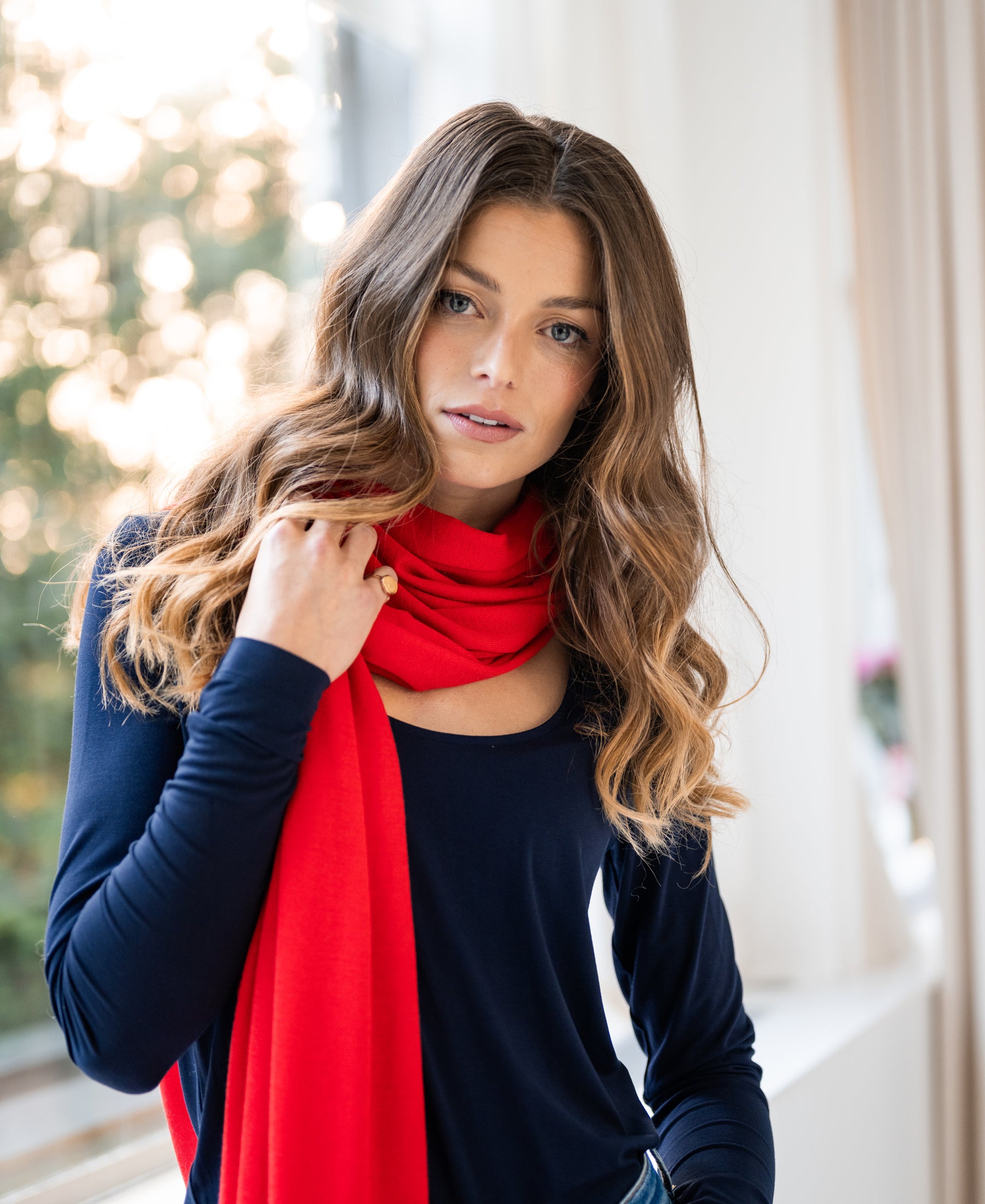 Woman wearing a navy blue LA CHARME T-shirt by PLEIN PUBLIQUE, standing indoors by a window.