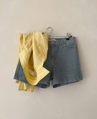 Yellow and white striped shirt called LA BILLY by PLEIN PUBLIQUE on hanger against light wall.