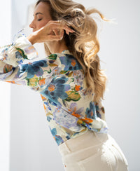 Light blue floral print blouse by PLEIN PUBLIQUE, shown on a model with sunlight on her wavy blonde hair.