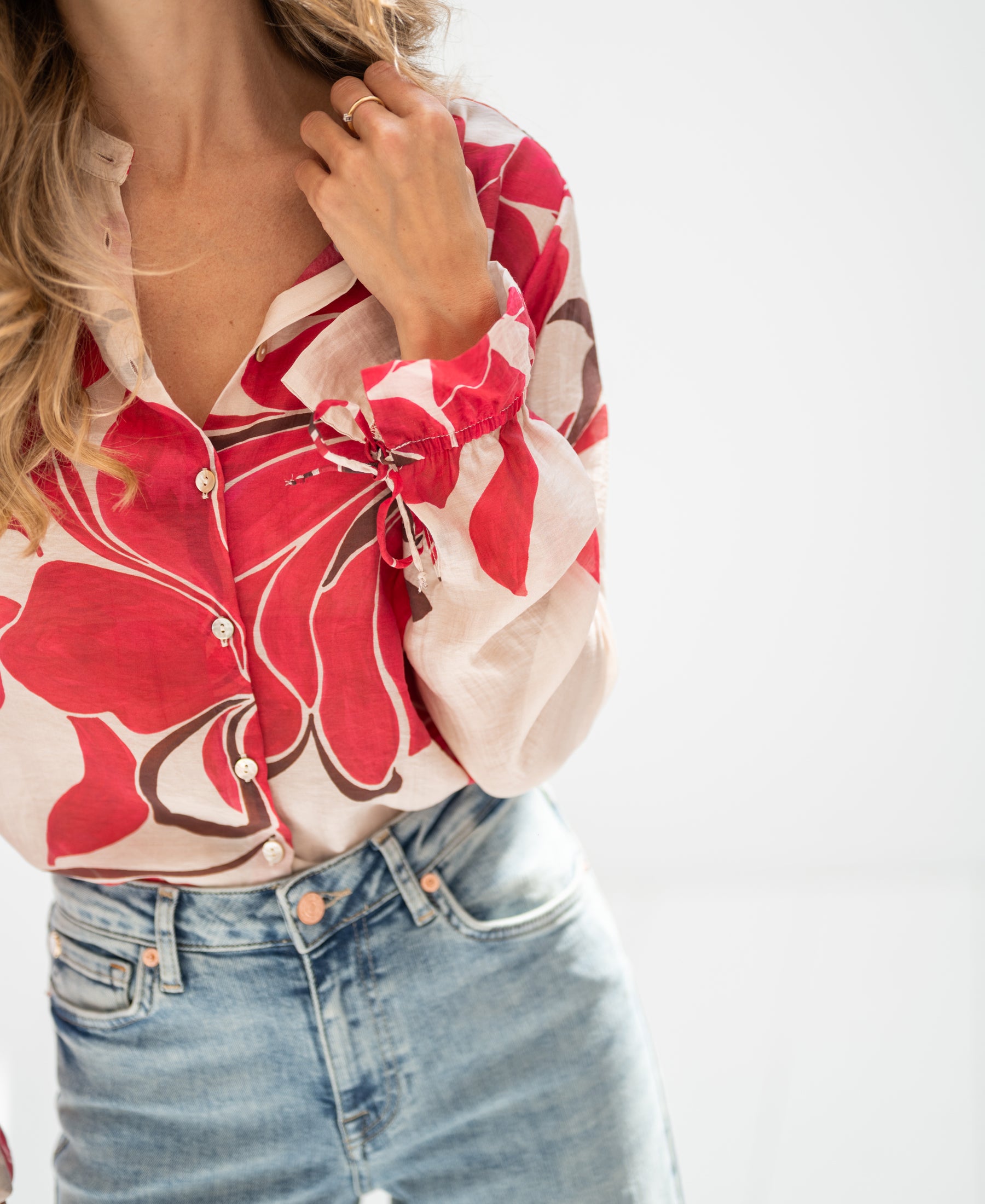 Woman wearing red print blouse with hand on collar, against white background.