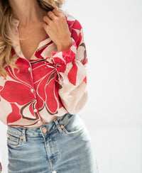 Woman wearing red print blouse with hand on collar, against white background.