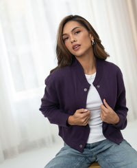 Dark purple bomber jacket in a cassis shade, shown indoors with model holding the lapels.