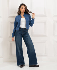 Woman poses in blue heritage wide leg jeans against white panel wall.