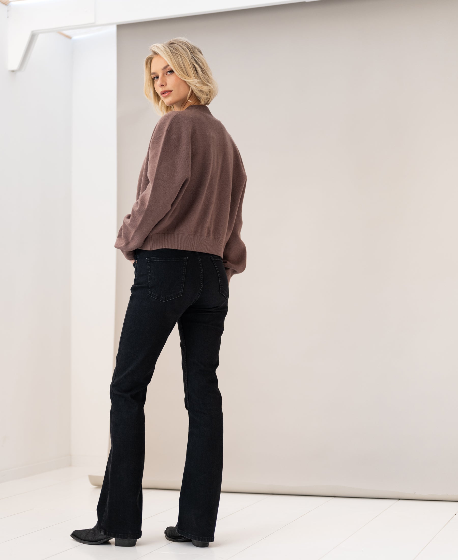 Woman wearing a PLEIN PUBLIQUE LA BOMBA Innuendo bomber jacket, standing in studio and looking over her shoulder.