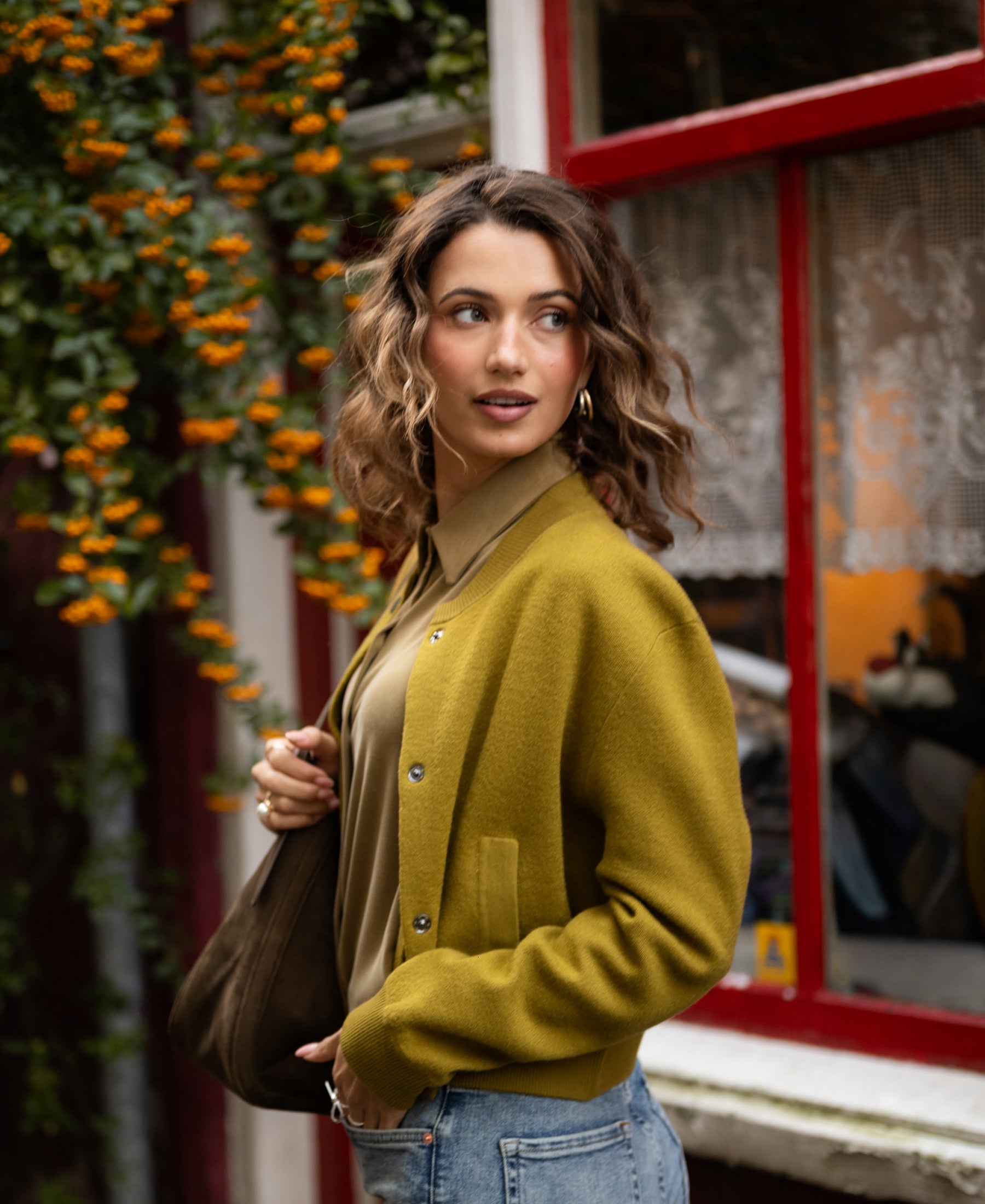 Woman wearing an olive green bomber jacket stands outside.