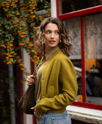Woman wearing an olive green bomber jacket stands outside.