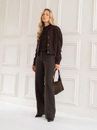 Women's brown bomber jacket in pure chocolate color, shown by a white paneled wall.