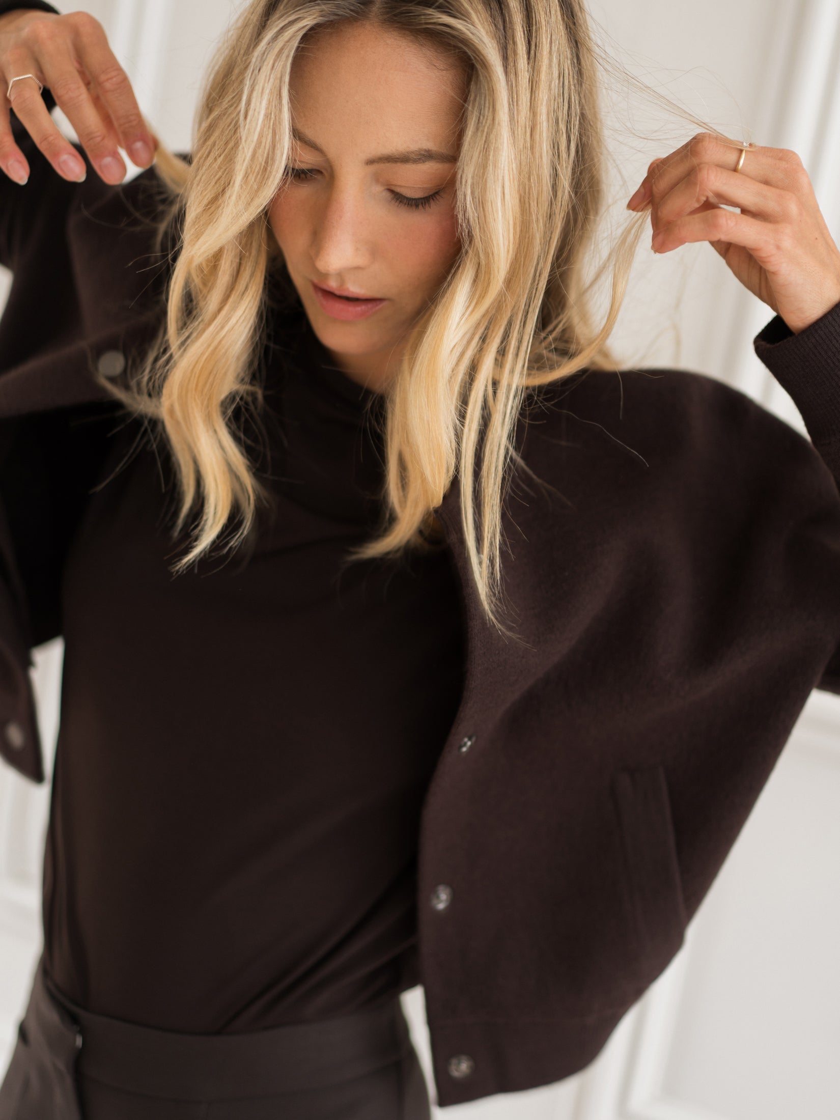 A woman adjusts the PLEIN PUBLIQUE chocolate brown bomber jacket.