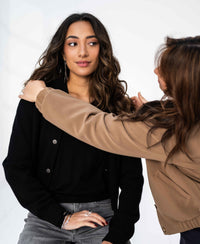 Woman wearing a black PLEIN PUBLIQUE LA BOMBA bomber jacket, shown on a plain backdrop.