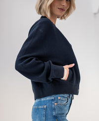 Dark blue LA BOMBA bomber jacket shown from the side with hands in pockets.
