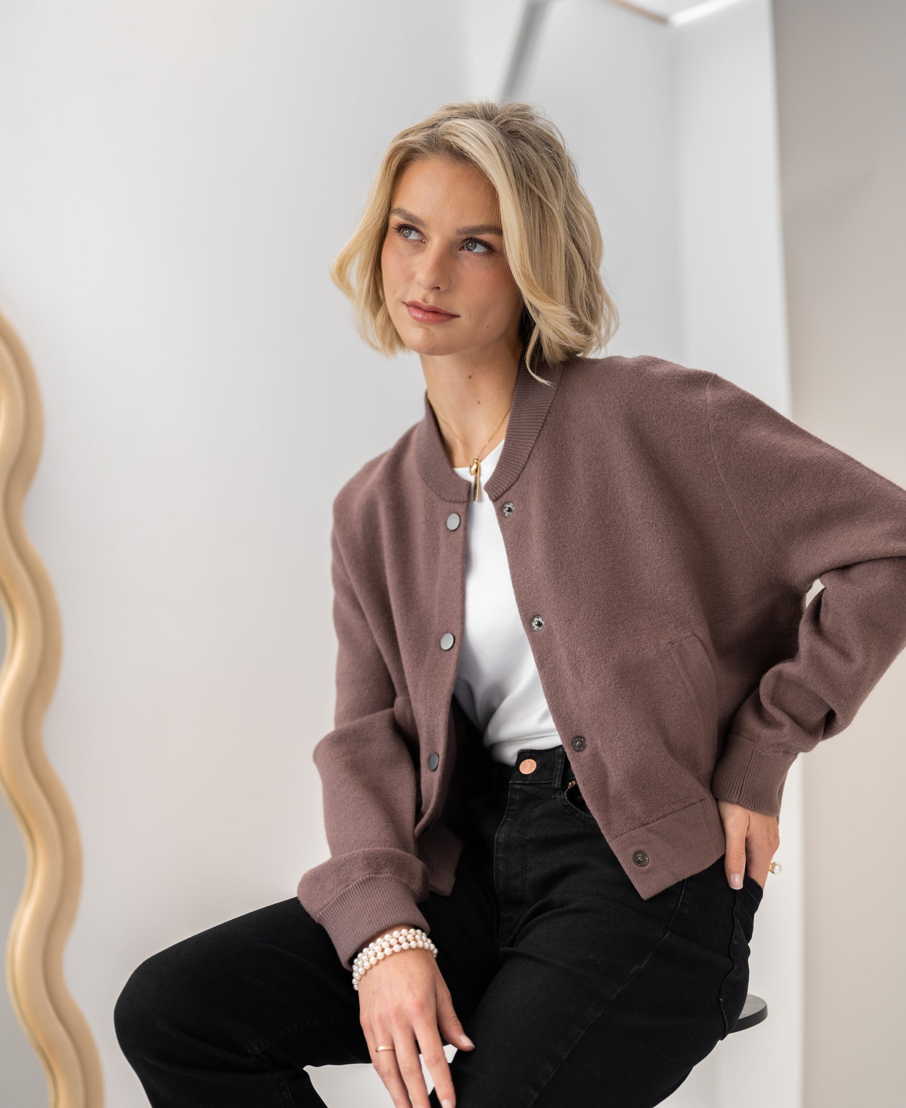 Woman wearing the PLEIN PUBLIQUE LA BOMBA bomber jacket in Innuendo sits, looking thoughtful.