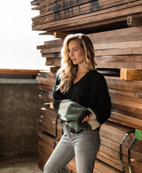 Woman wearing a PLEIN PUBLIQUE fluffy black striped vest stands leaning on wooden boards.
