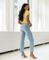 Woman wearing bleached cropped jeans stands indoors sideways with hands in back pockets.