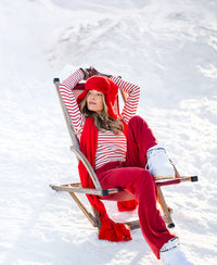 Red PLEIN PUBLIQUE lounge pants, LE HUGO Rouge, shown worn outdoors on a chair in snowy sunlight.