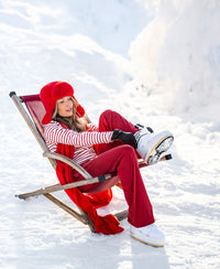Woman wearing red LE HUGO Lounge pants sits on a wooden chair in the snow.