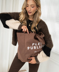 Brown canvas tote bag with text on the front, by PLEIN PUBLIQUE, shown from above.