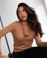 Chai tea colored waterfall neck sweater in soft knit, shown indoors on a model with long wavy hair, side view.