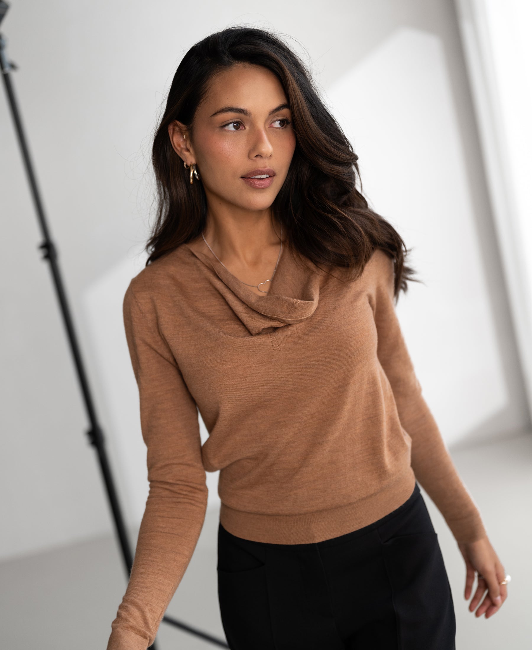 Woman wears Plein Publique LA CASCADE waterfall neck sweater in chai tea color indoors.