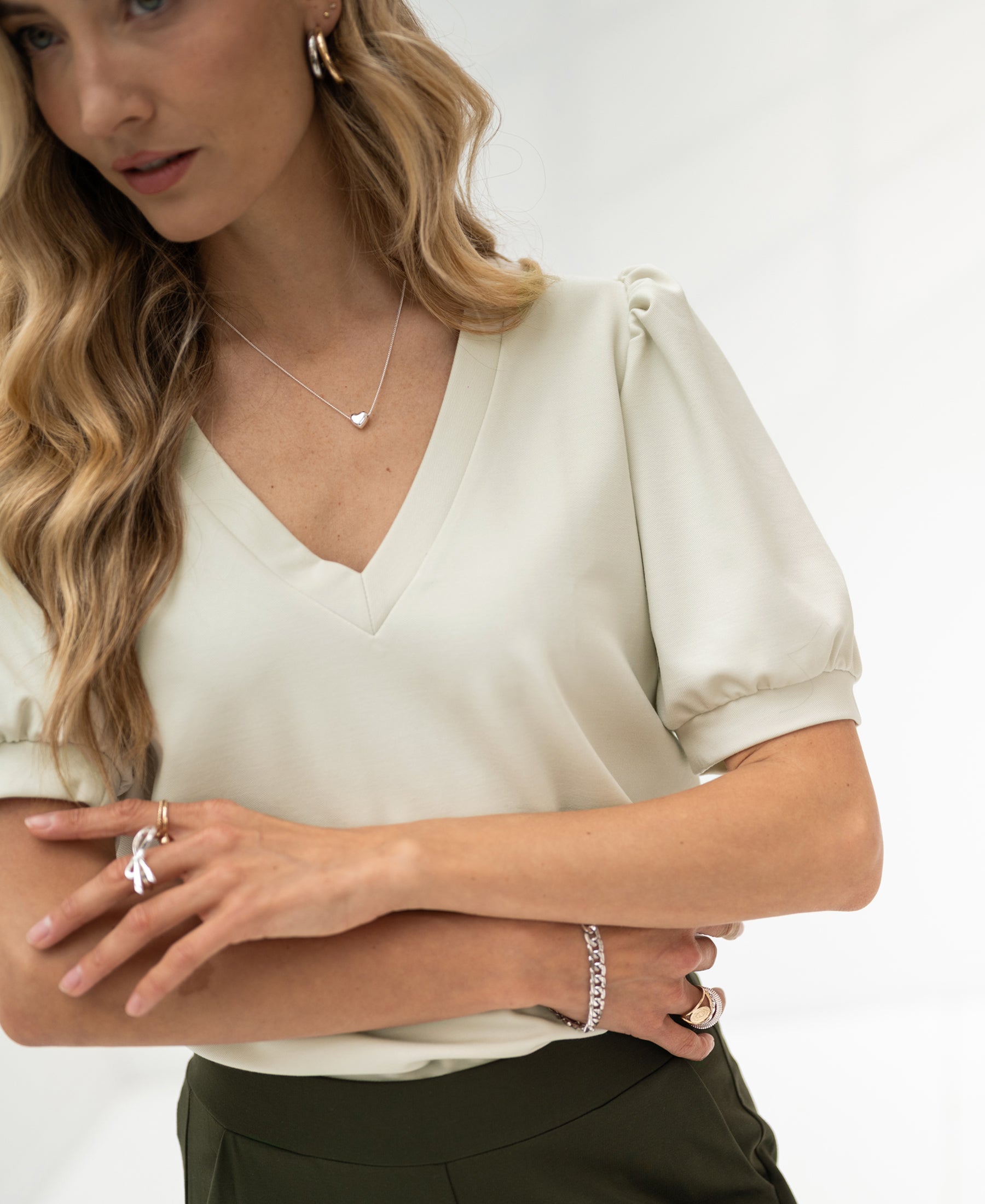 Stone-colored LA CELINE Traveltop by OVERIG with puff sleeves, worn by model, arms crossed, blurred background.