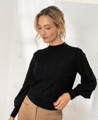 Woman wearing a black PLEIN PUBLIQUE turtleneck sweater with beaded details, standing indoors and looking down.