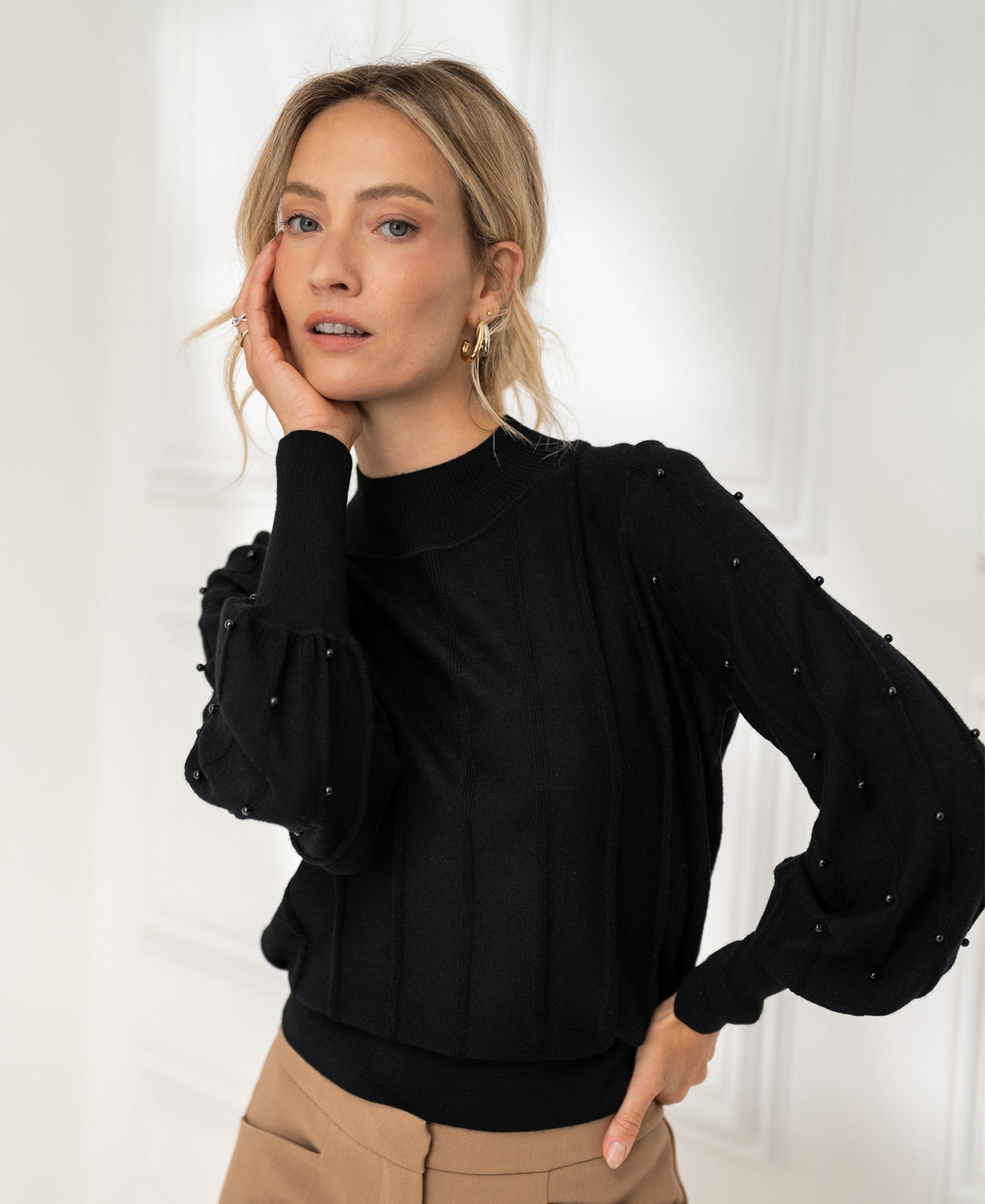 Woman wearing a black turtleneck sweater with beaded details by PLEIN PUBLIQUE, indoors.