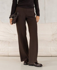 Wide-leg brown trousers displayed on a person standing by a light sofa.