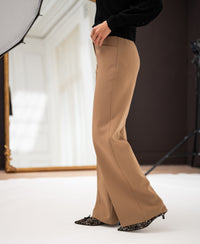 Woman wearing camel wide-leg pants in a studio with a large mirror behind.