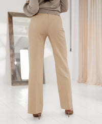 Wide-leg pants in light sand color, back view; woman indoors with a mirror behind.