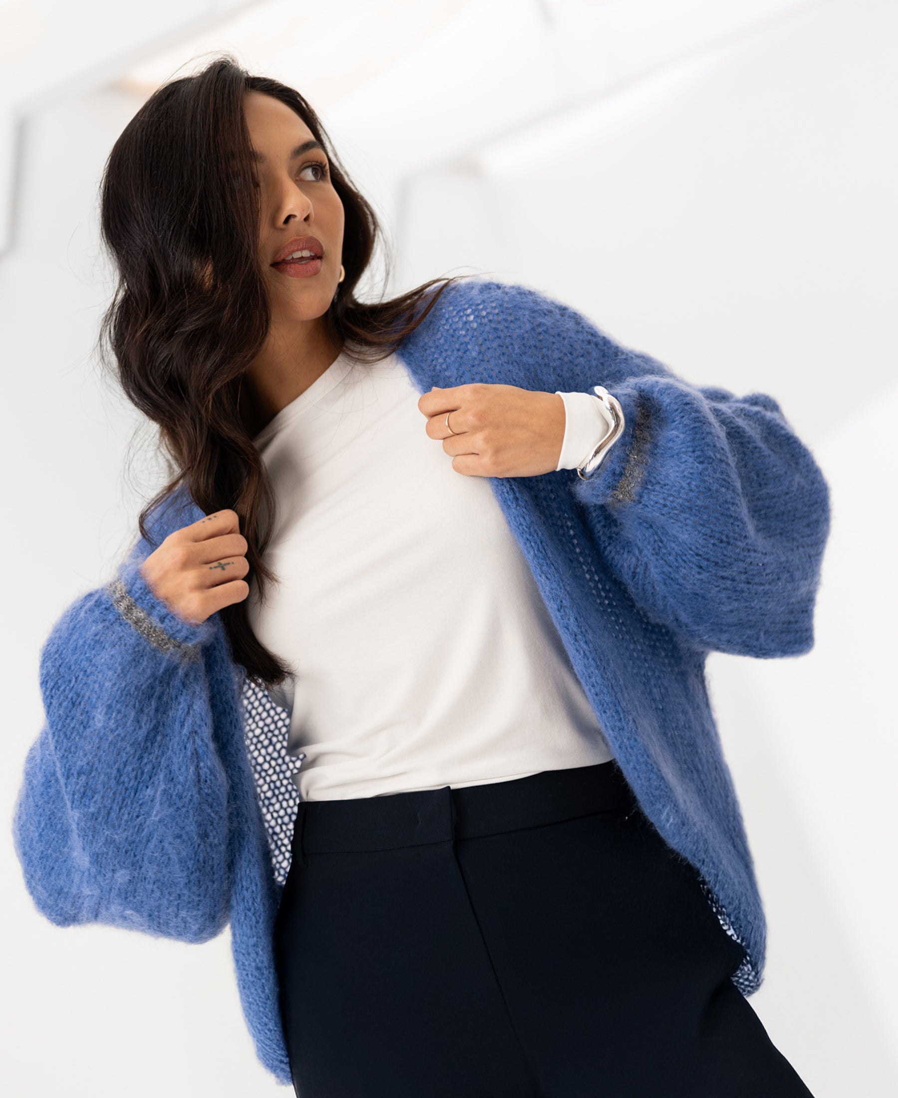 Woman wearing a blue fluffy vest, standing indoors and looking to the side.