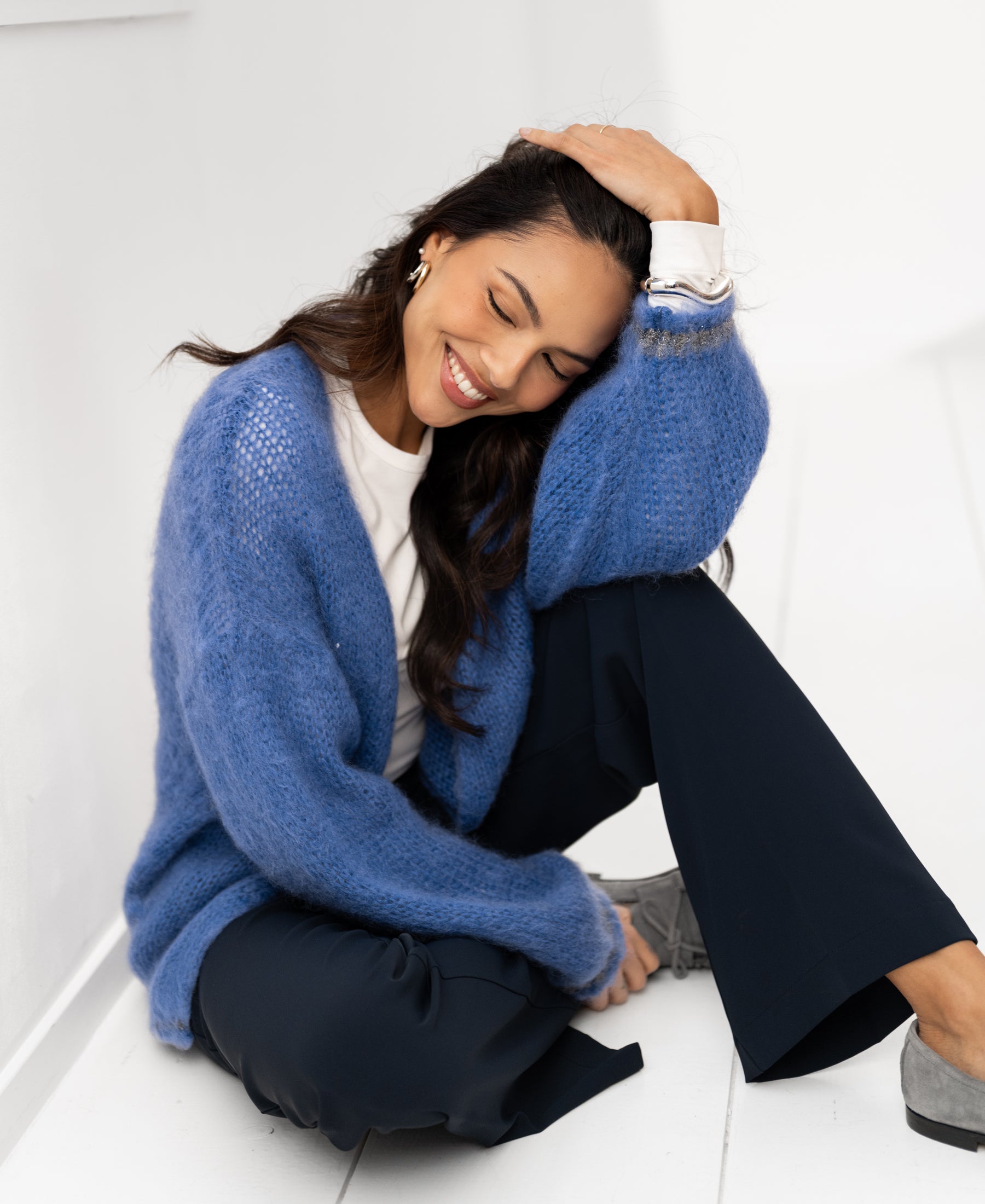Woman with eyes closed, smiling and resting her head on her hand, wearing the blue Fluffy vest LA CHERIE by PLEIN PUBLIQUE.