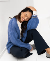 Woman with eyes closed, smiling and resting her head on her hand, wearing the blue Fluffy vest LA CHERIE by PLEIN PUBLIQUE.