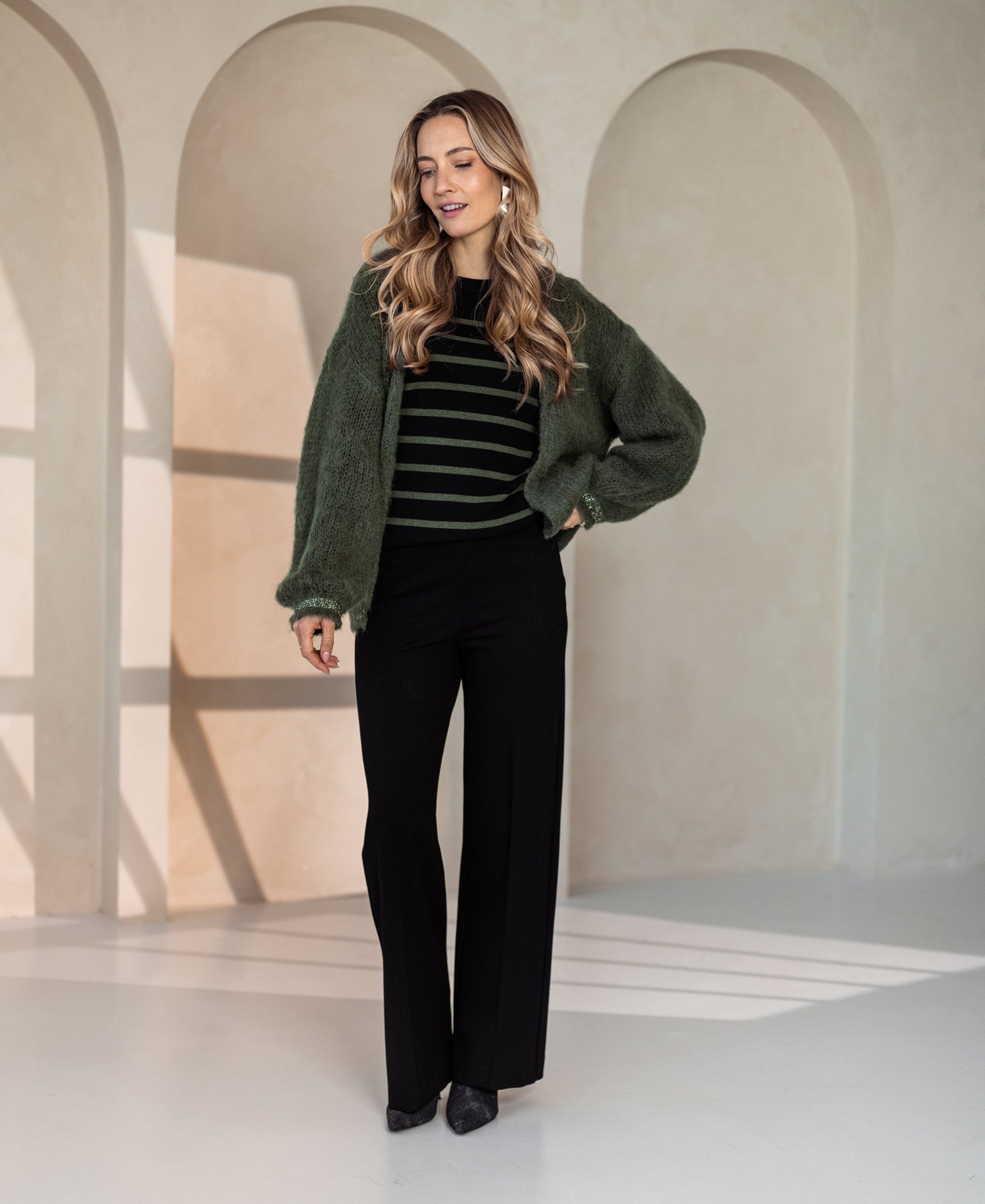 Woman wearing a black and army green sweater dress in a sunlit room.