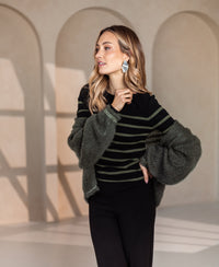 L'ELISA black and army green dress by PLEIN PUBLIQUE, shown in a sunlit room with arched walls.