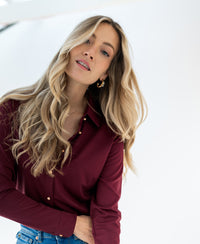 Woman wearing a Plein Publique travel blouse in cherry wine color stands against a white background.