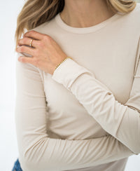 Woman wearing the PLEIN PUBLIQUE Luxe undershirt LE CHOLET in light sand, hand resting on her shoulder.