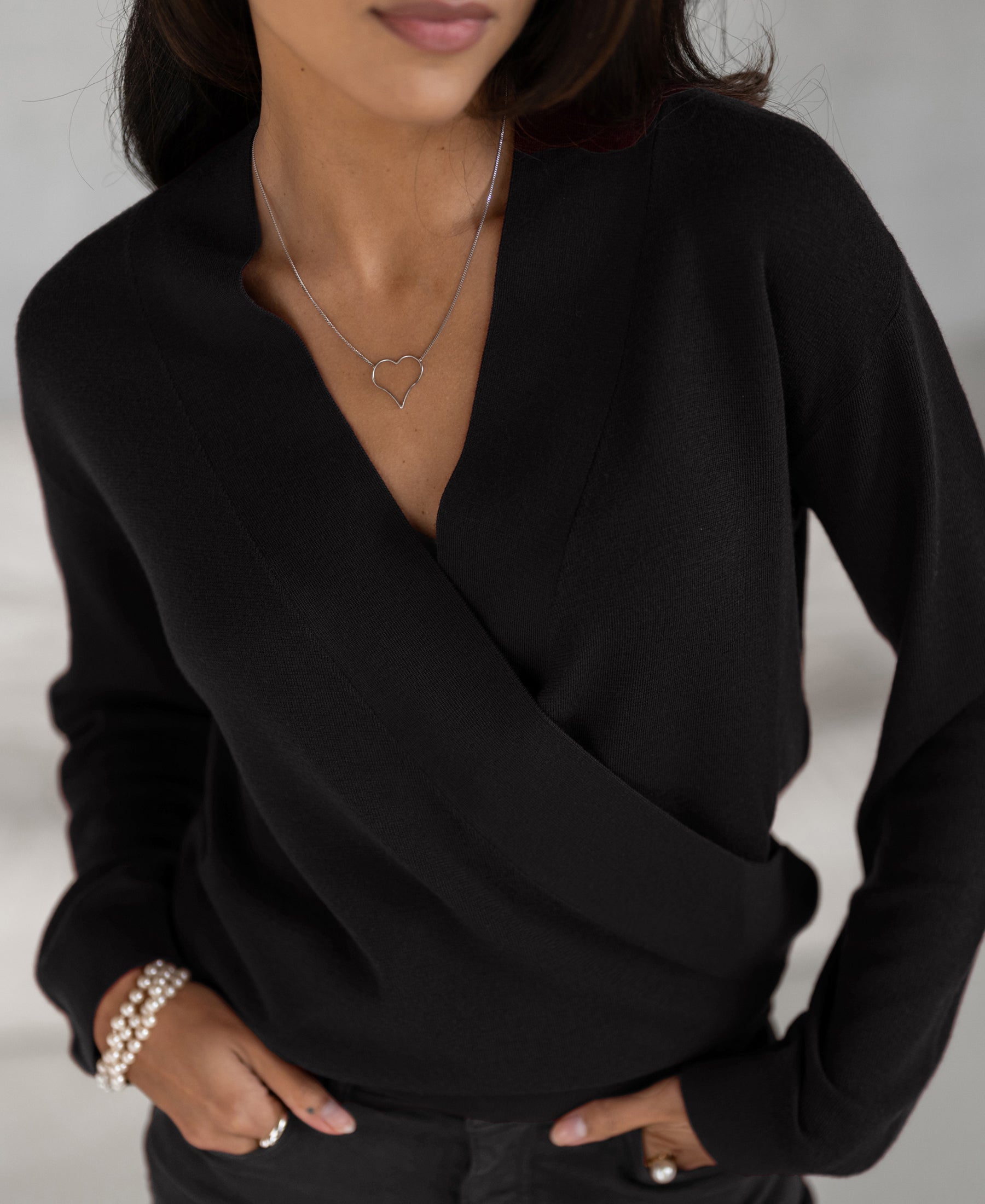 Woman wearing black LES CINQ wrap sweater by PLEIN PUBLIQUE, hands in pockets.