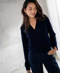 Woman wearing a navy blue LES CINQ wrap sweater by PLEIN PUBLIQUE, standing indoors with one hand in her pocket.