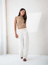 Sleeveless polo sweater in soft camel by PLEIN PUBLIQUE, shown in a bright, minimalist room.