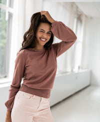 Dusty pink merino wool sweater LA COEUR by PLEIN PUBLIQUE shown on model standing by large windows.