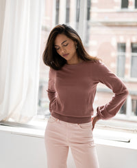 Woman wearing a dusty pink merino wool sweater, viewed by a window.
