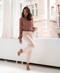 Woman indoors by a window poses in a dusty pink merino wool sweater, one leg raised.