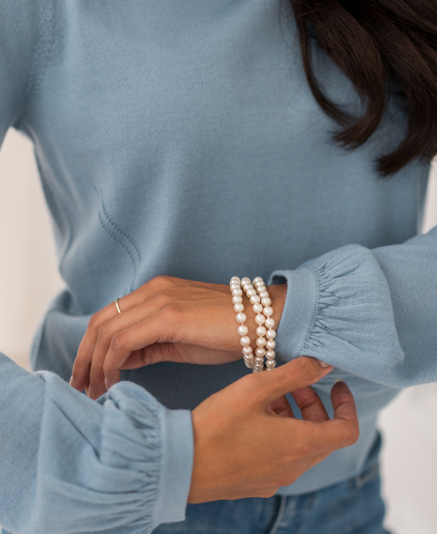 Woman wearing light blue LA COEUR Merino wool sweater by PLEIN PUBLIQUE, adjusting her sleeve.