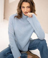Woman wearing a light blue PLEIN PUBLIQUE LA COZY turtleneck sweater.