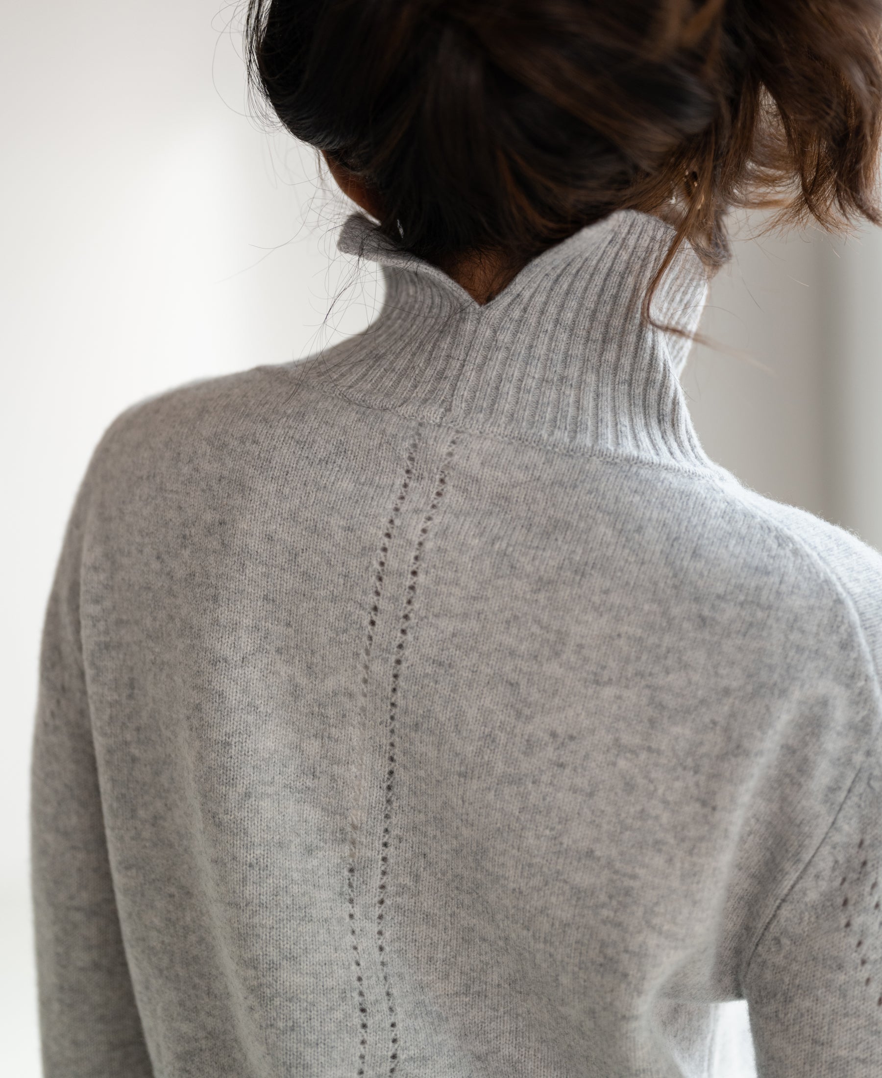Back view of a person wearing a grey turtleneck sweater.
