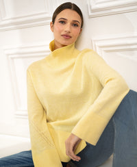 Yellow LA COZY Citron Pressed turtleneck sweater by PLEIN PUBLIQUE, shown on a model sitting against a white wall.