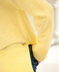 Person wearing a LA COZY lemon yellow turtleneck sweater with a small gold heart pin near the hem.