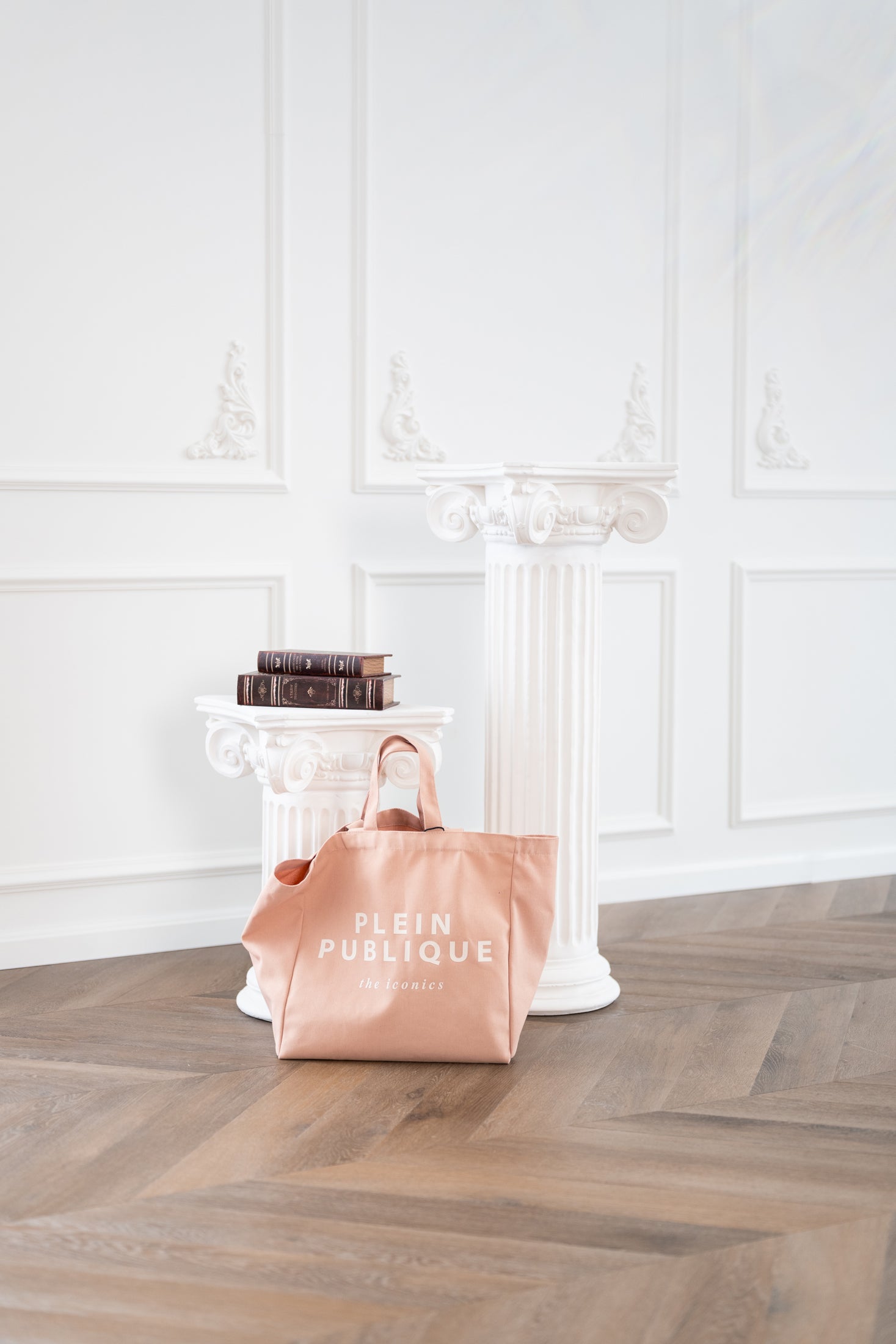Blush canvas tote bag by Plein Publique displayed on white columns in an elegant, white-walled room.