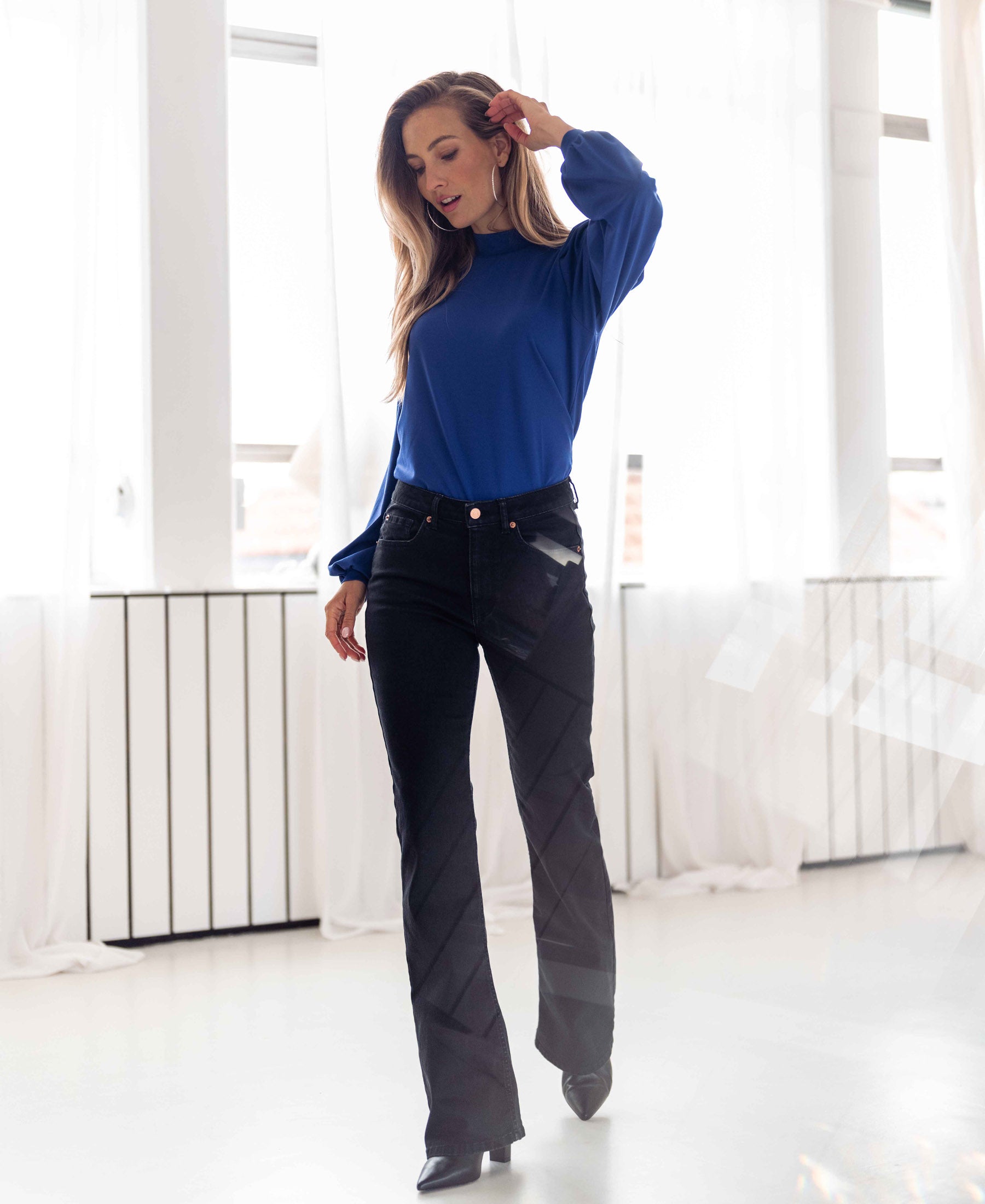Black denim flared jeans shown in a bright room with white curtains.