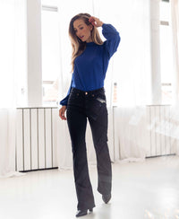 Black denim flared jeans shown in a bright room with white curtains.